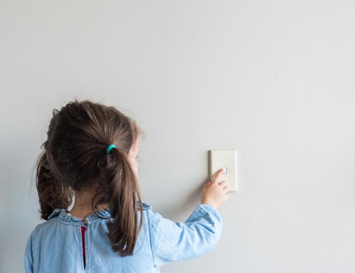 A little girl turning on a light switch on the wall