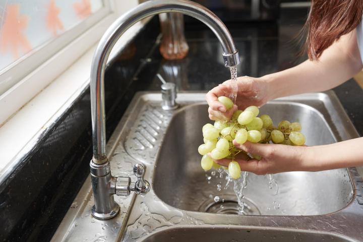 A woman standing at a kitchen sink, washing grapes under tap.