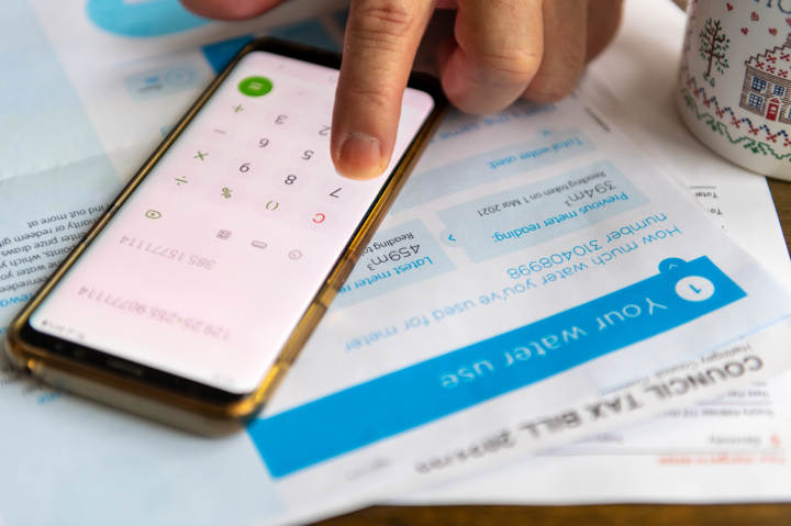 A water bill on a table, with a person's hand using a smartphone's calculator app