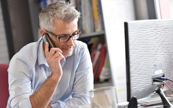 A photo of a man on the phone, looking at his computer screen